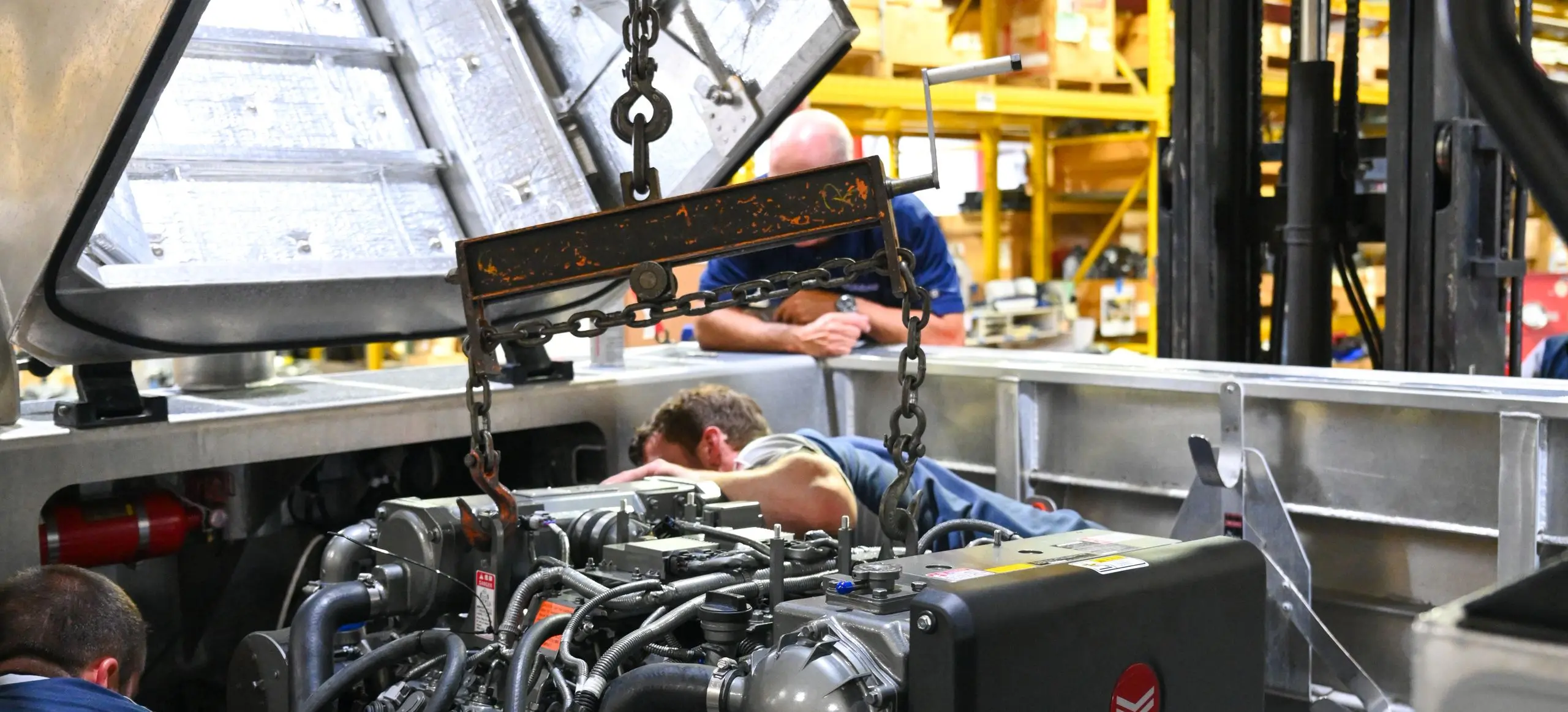 Marine diesel engine lowered into a hull on a chain hoist during a repower